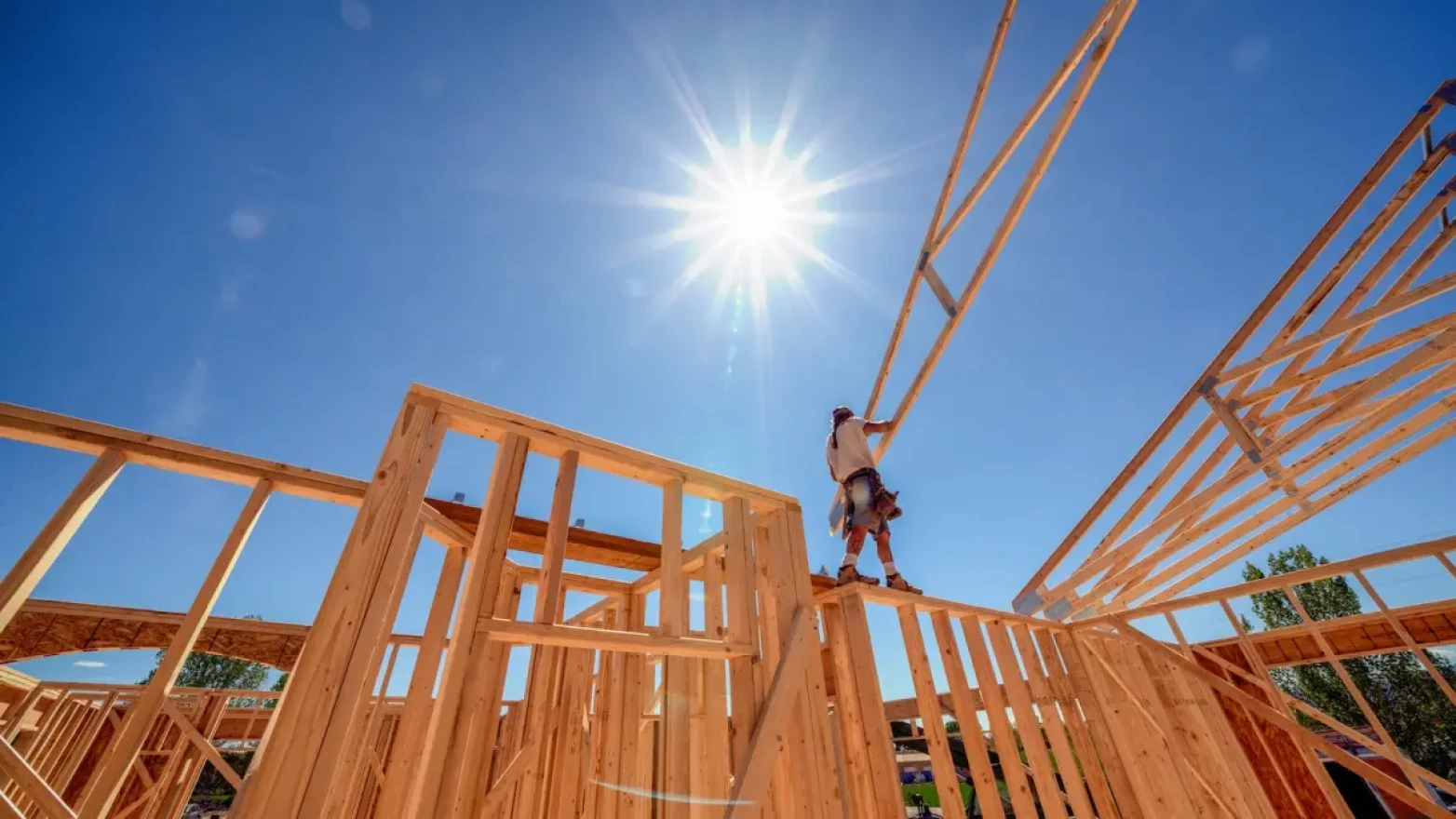 A man walking on top of the wood frame for a house.